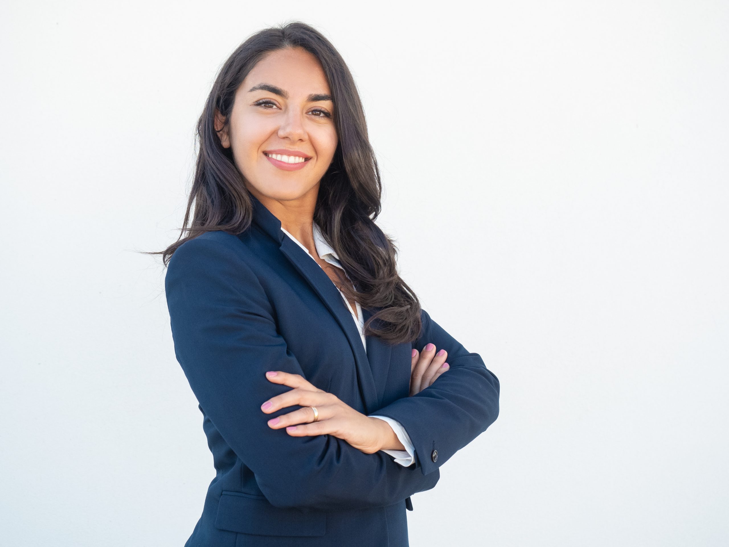 Smiling confident businesswoman posing with arms folded. Happy beautiful black haired young Latin woman in formal suit standing for camera over white studio background. Corporate portrait concept